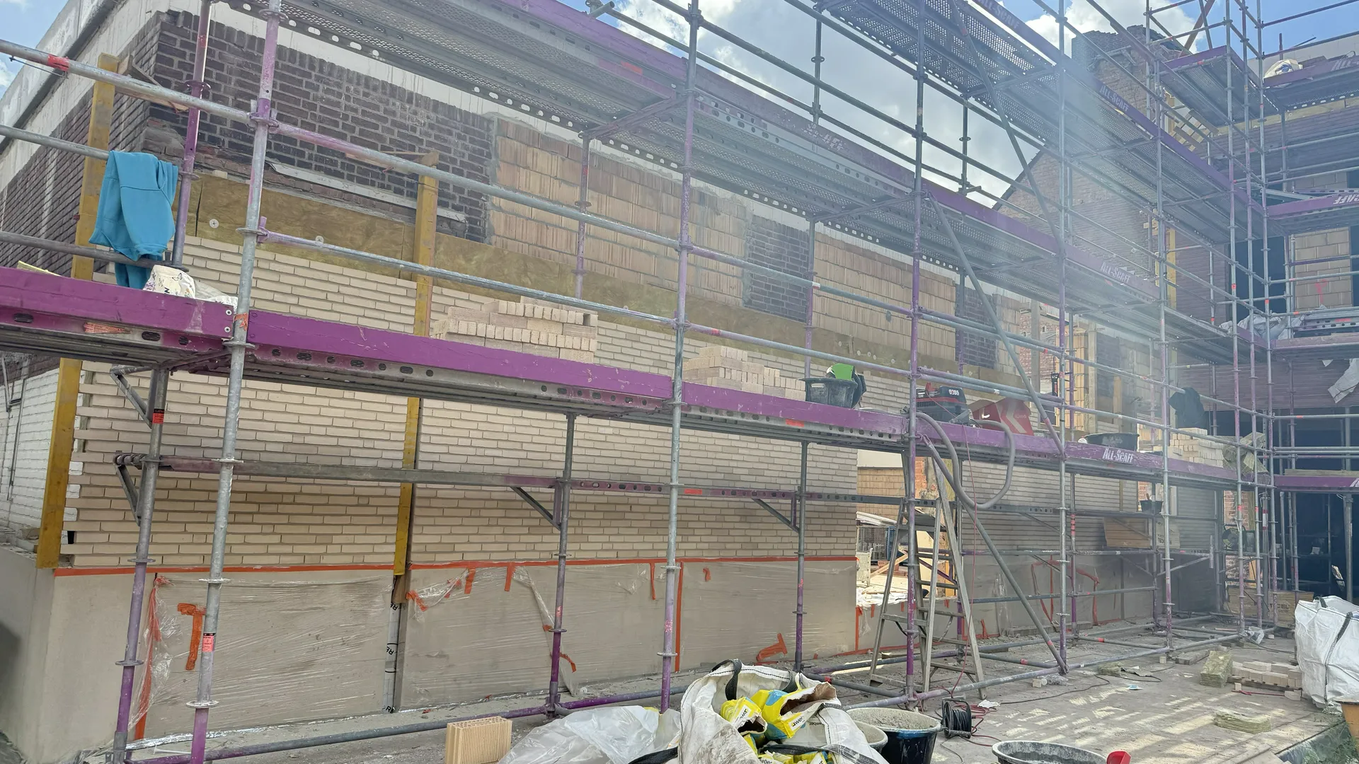 Prace nad elewacją domu – układanie jasnych cegieł na ścianie z rusztowaniem Elewacje domu