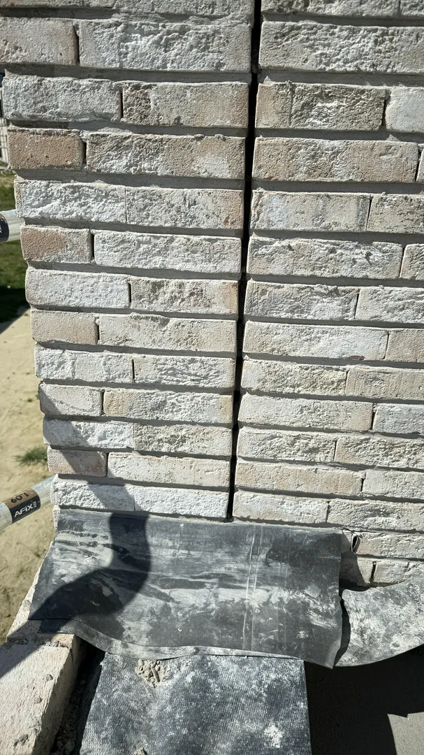 Montaż elewacji domu z białej cegły elewacyjnej na izolacji fundamentów z papy termozgrzewalnej