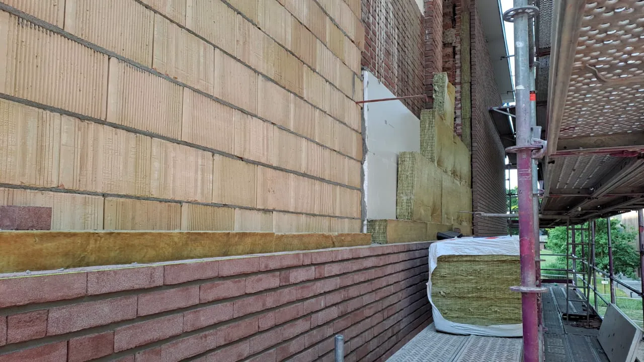 Montaż elewacji domu z izolacją termiczną wełny mineralnej i ceglaną okładziną, widoczne rusztowanie