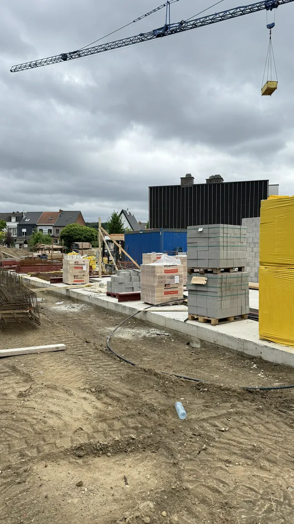 Płyta fundamentowa z paletami bloczków betonowych i żurawiem w tle