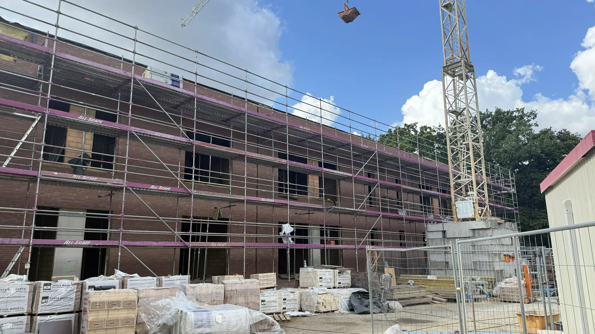 Elewacje domu z ceglaną ścianą w budowie, rusztowanie i palety materiałów