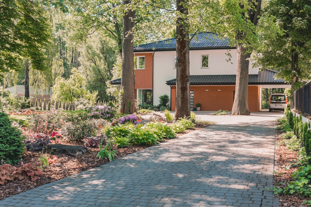 Podjazdy i chodniki z kostki brukowej prowadzące do nowoczesnego domu jednorodzinnego otoczonego zielenią