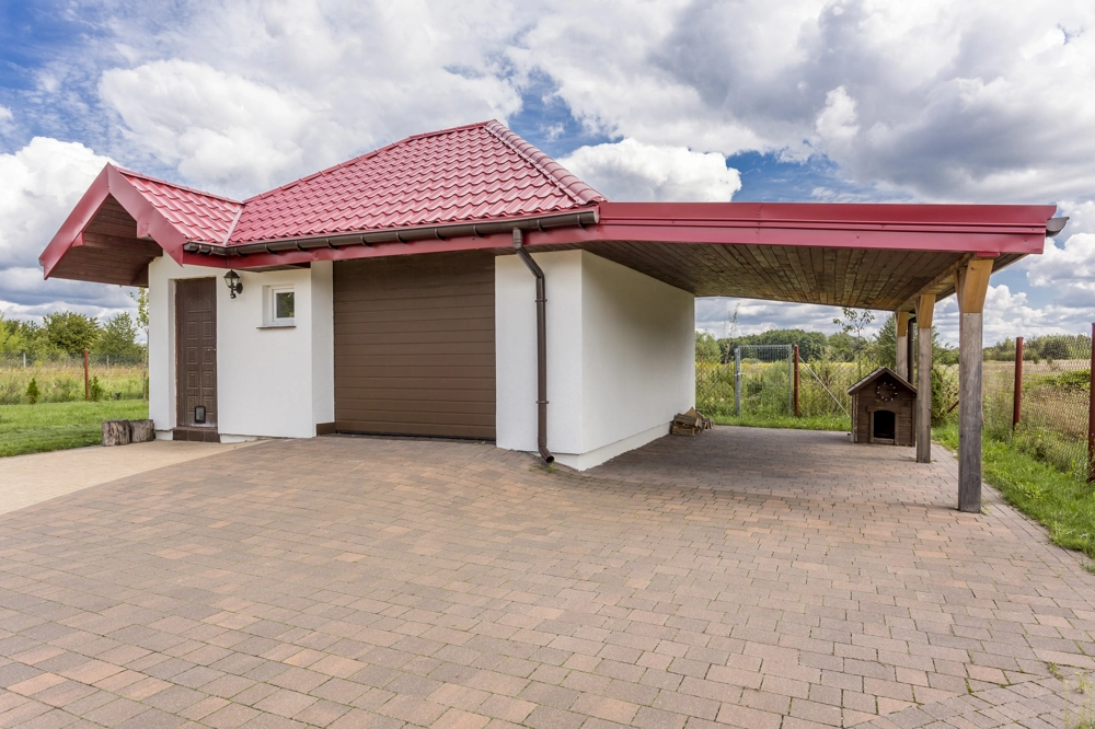 Carport z czerwoną blachodachówką i podjazdem z kostki brukowej