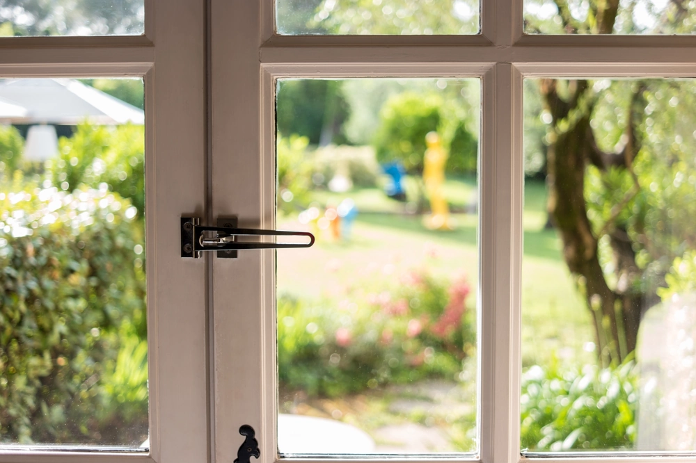 Drzwi balkonowe z metalowym zaczepem zabezpieczającym i przeszklonym panelem, widok na ogród