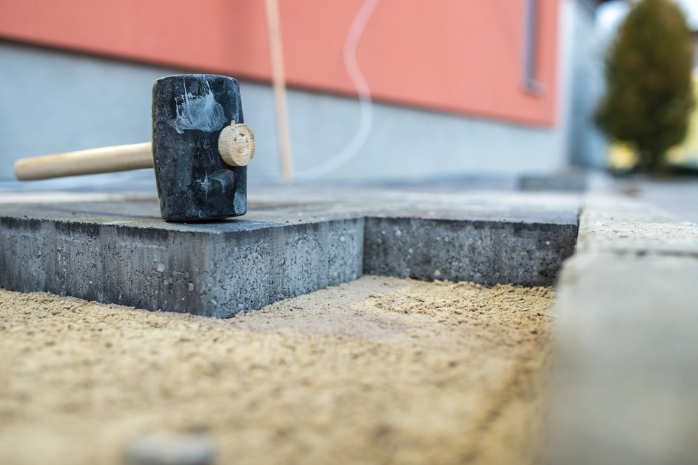 Układanie kostki brukowej: młotek kauczukowy na betonowej płycie i podsypce piaskowej
