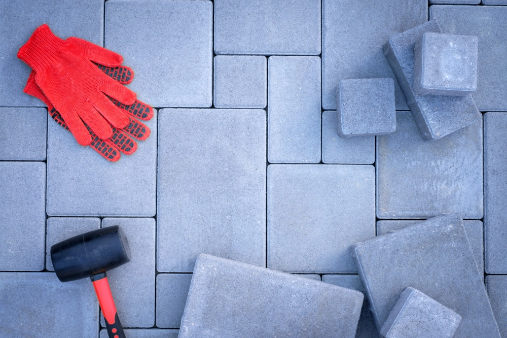 Czerwone rękawice i gumowy młotek na rozłożonych szarych kostkach brukowych – układanie kostki brukowej