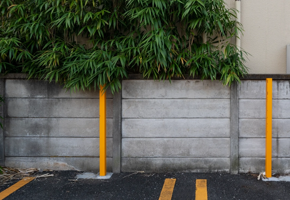 Betonowe ogrodzenie z żółtymi słupkami ochronnymi i parkingową nawierzchnią